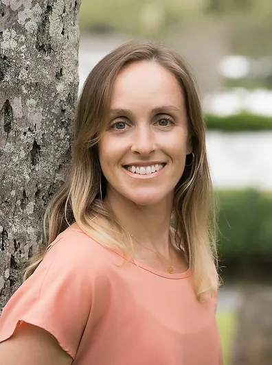 headshot of Mariya Gold wearing peach shirt standing against tree smiling